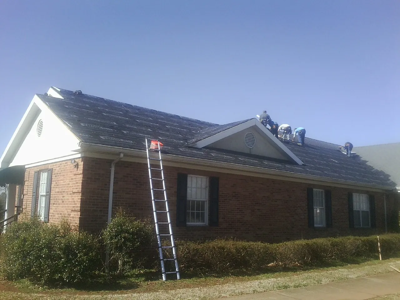 Crew tearing shingles off a brick ranch roof with a ladder set — Emergency Roof Repair work by our crew in Fort Klamath