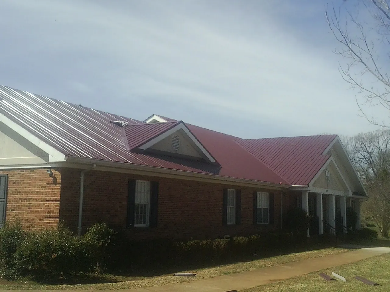 Red metal roof with gabled entries on a long brick building, from a Hail Damage Roof Repair job in Fort Klamath