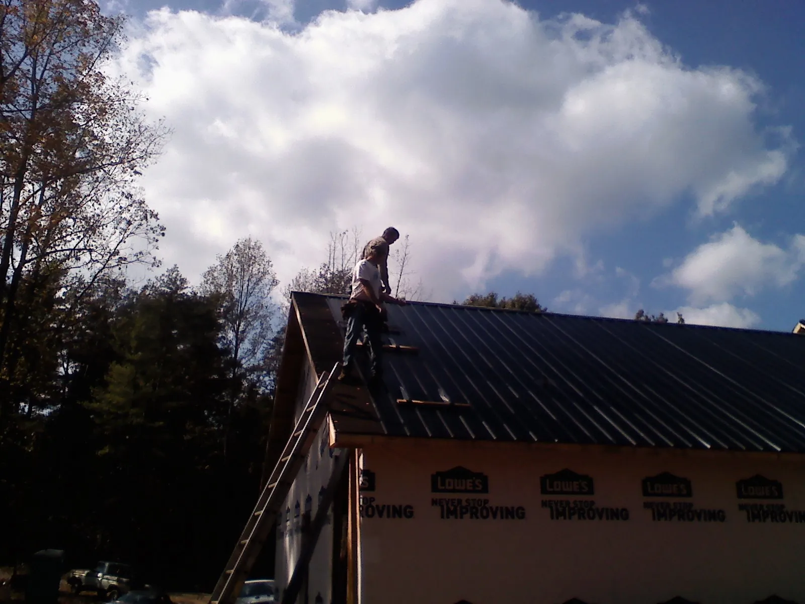 Roofer fastening dark metal panels high against a cloudy sky, from a Roof Inspection job in Fort Klamath