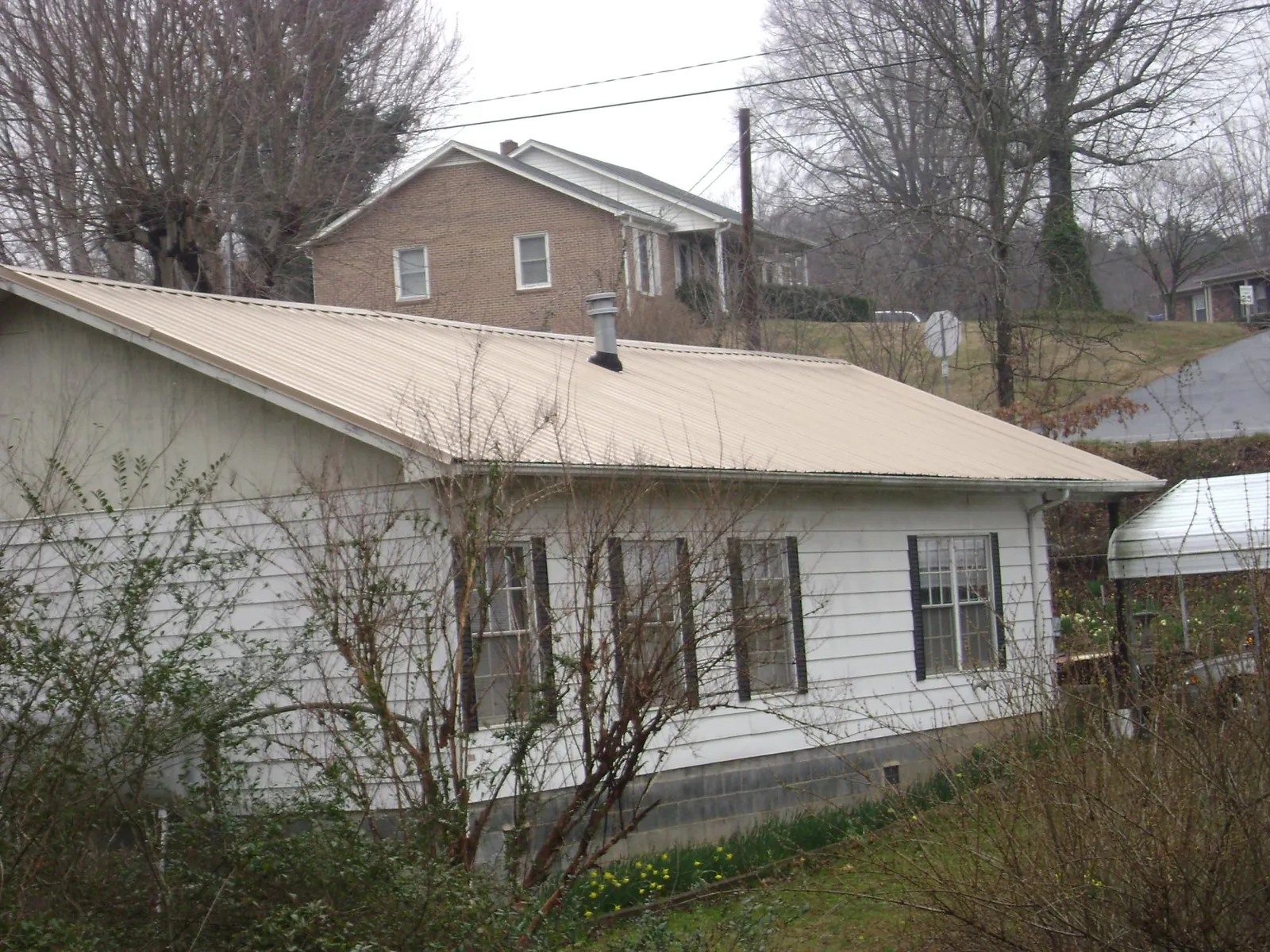 Tan metal roof on a white sided house set into a hillside — Commercial Roofing by Roofing Brothers in Fort Klamath